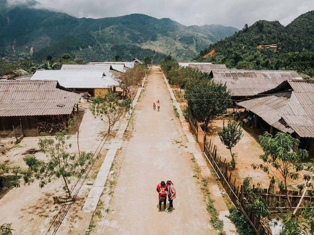 The main path through Cu Vai Village, lined with wooden houses, with villagers walking, Tram Tau, Yen Bai