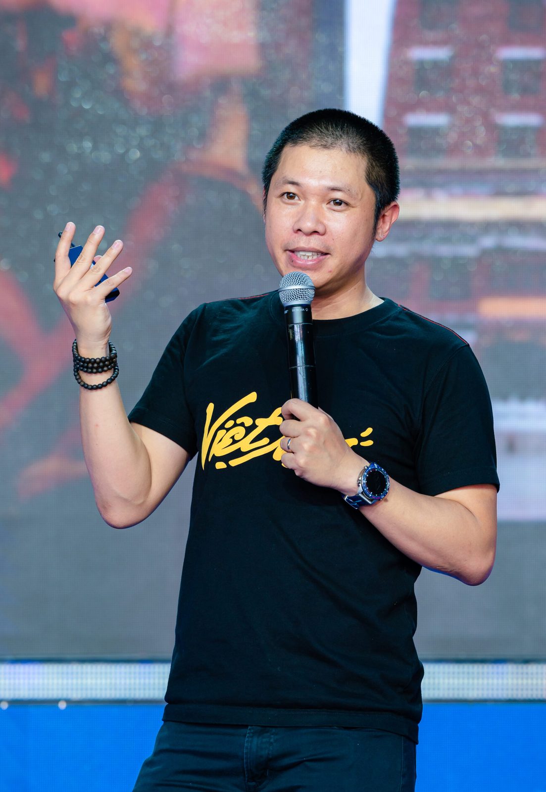 Nguyễn Tiến Huy speaking on stage with a microphone